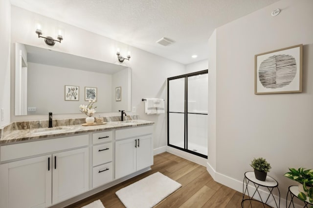 bathroom featuring vanity, hardwood / wood-style flooring, a textured ceiling, and a shower with door