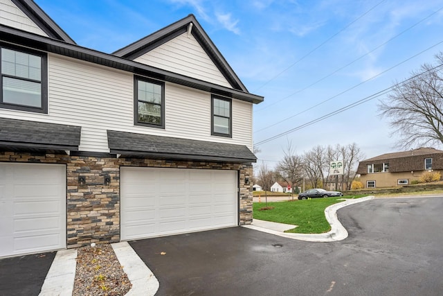 view of side of property with an attached garage, stone siding, aphalt driveway, and roof with shingles