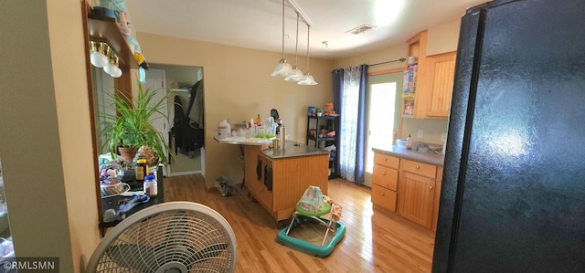 kitchen featuring a kitchen island with sink, light hardwood / wood-style floors, black refrigerator, light brown cabinets, and decorative light fixtures