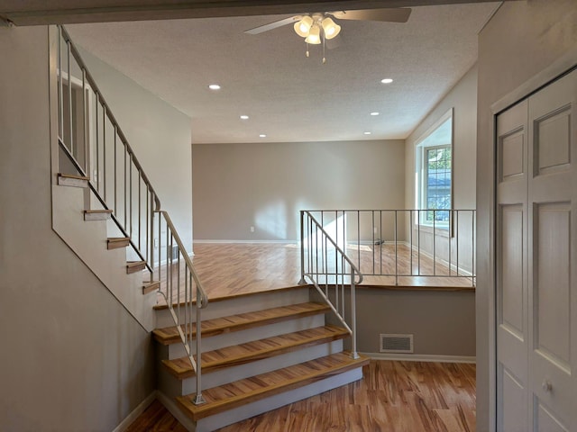 staircase featuring a textured ceiling, hardwood / wood-style flooring, and ceiling fan