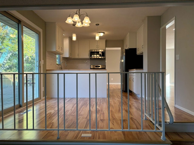 kitchen featuring appliances with stainless steel finishes, white cabinets, hanging light fixtures, and light hardwood / wood-style floors