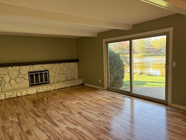 unfurnished living room featuring beam ceiling, a stone fireplace, a textured ceiling, and light hardwood / wood-style floors