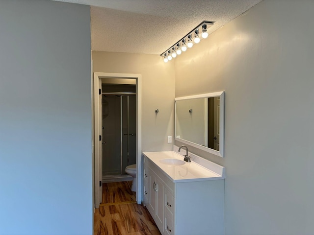 bathroom with a textured ceiling, an enclosed shower, hardwood / wood-style floors, toilet, and vanity