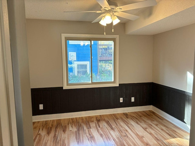 unfurnished room featuring a textured ceiling, wooden walls, light wood-type flooring, and ceiling fan