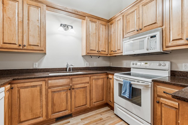 kitchen featuring sink, dark stone counters, white appliances, and light hardwood / wood-style flooring