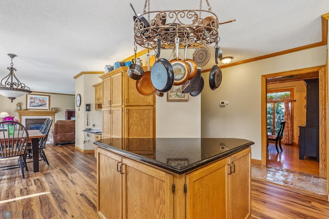 kitchen with light wood-type flooring, a textured ceiling, hanging light fixtures, and dark stone counters