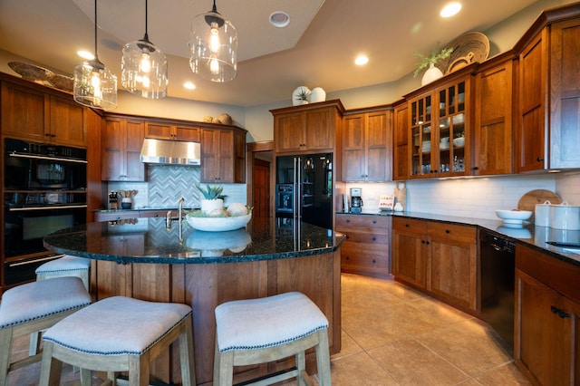 kitchen with tasteful backsplash, hanging light fixtures, a center island with sink, and black appliances