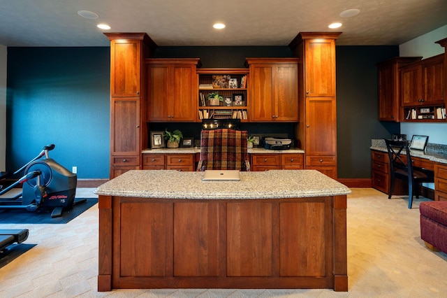 kitchen featuring a kitchen island, built in desk, and light stone counters