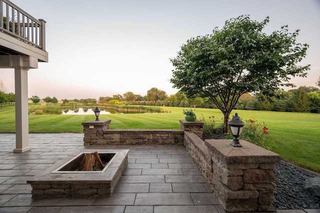 patio terrace at dusk featuring a yard, a fire pit, and a balcony