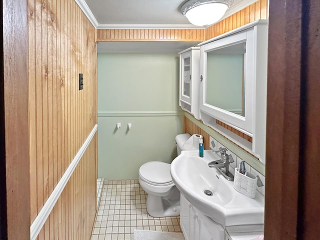 bathroom with wood walls, toilet, ornamental molding, and sink