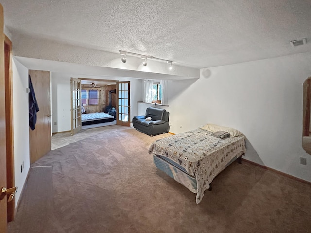 carpeted bedroom with french doors, rail lighting, and a textured ceiling