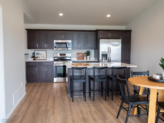 kitchen with dark brown cabinets, stainless steel appliances, and light hardwood / wood-style floors