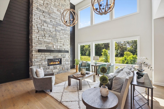 living room featuring light hardwood / wood-style floors, a stone fireplace, a towering ceiling, and an inviting chandelier