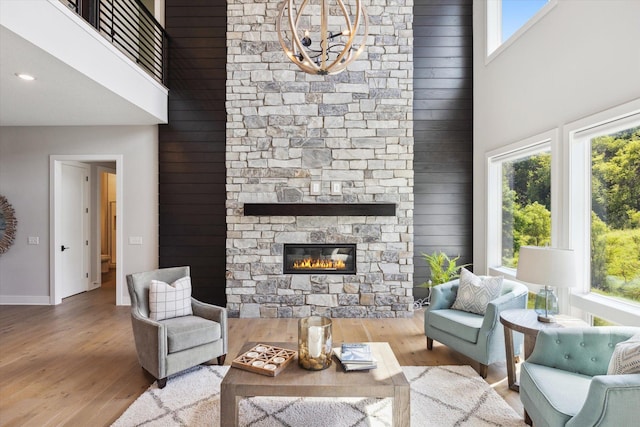 living room with a stone fireplace, a healthy amount of sunlight, wood-type flooring, and a high ceiling