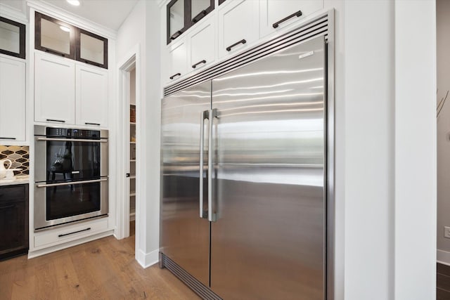 kitchen with decorative backsplash, white cabinetry, stainless steel appliances, and hardwood / wood-style flooring