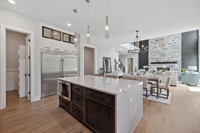 kitchen featuring built in appliances, hanging light fixtures, light stone countertops, a fireplace, and light hardwood / wood-style floors