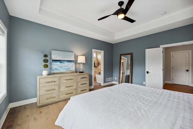 bedroom featuring a raised ceiling, ceiling fan, light hardwood / wood-style floors, connected bathroom, and crown molding