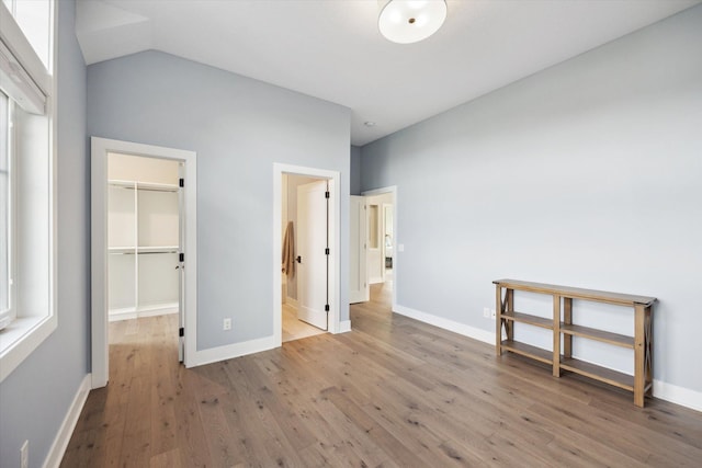 unfurnished bedroom with a closet, wood-type flooring, lofted ceiling, and a walk in closet