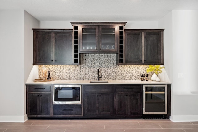 bar with stainless steel microwave, dark brown cabinets, backsplash, wine cooler, and sink