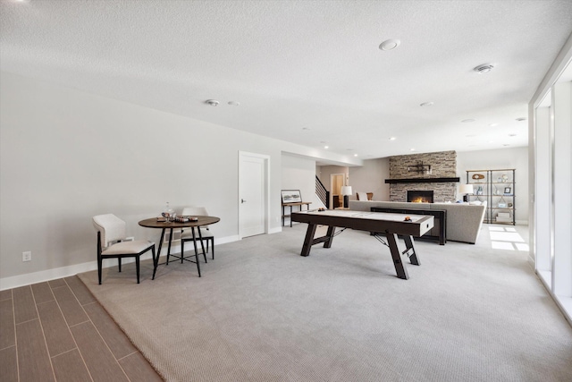 rec room with a stone fireplace, a textured ceiling, and carpet