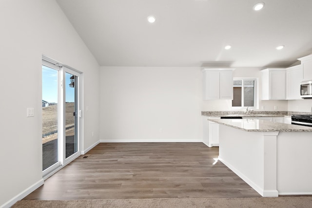 kitchen featuring black gas range, vaulted ceiling, hardwood / wood-style flooring, and white cabinetry