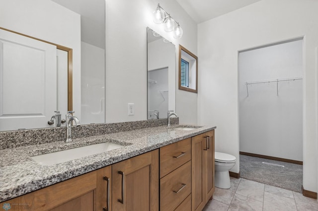 bathroom featuring double vanity, a sink, baseboards, and a walk in closet