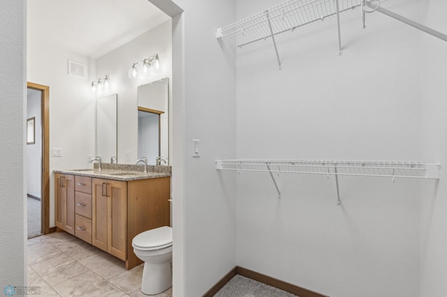 full bath with double vanity, a sink, baseboards, toilet, and marble finish floor