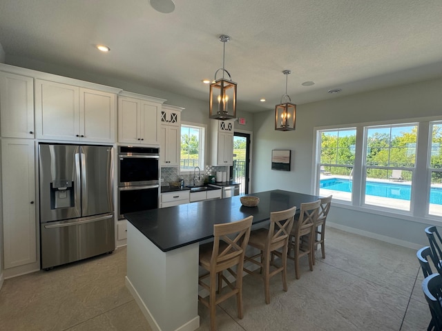 kitchen with stainless steel appliances, dark countertops, a sink, baseboards, and decorative backsplash