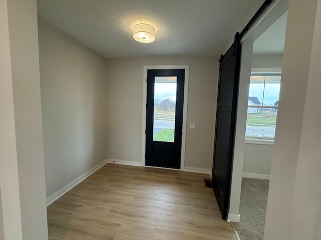 entryway featuring a barn door, baseboards, light wood-type flooring, and a textured ceiling