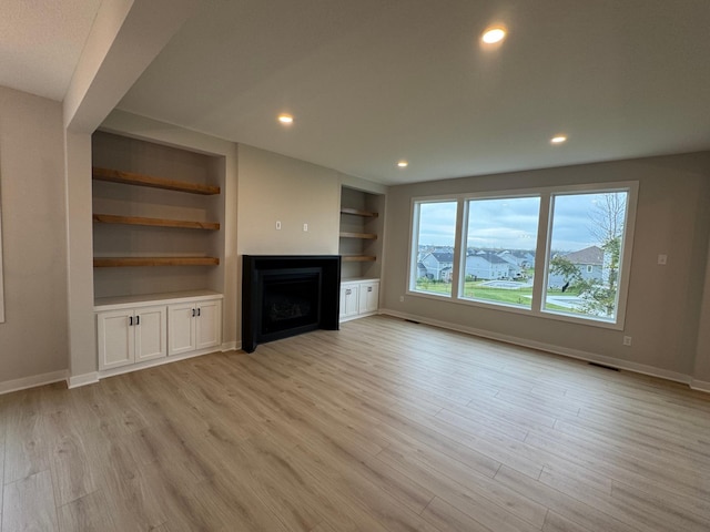 unfurnished living room featuring built in features and light wood-type flooring