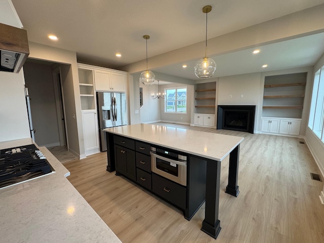 kitchen with stainless steel appliances, dark cabinetry, light wood-style flooring, built in features, and open shelves