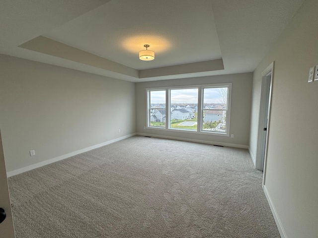 spare room featuring a raised ceiling, carpet floors, and baseboards