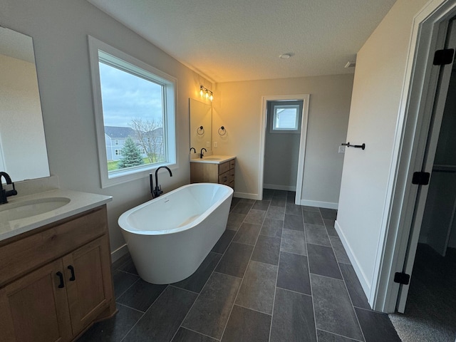 full bathroom featuring a freestanding bath, two vanities, baseboards, and a textured ceiling