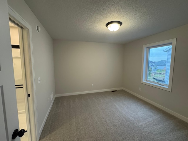 spare room with carpet floors, a textured ceiling, and baseboards