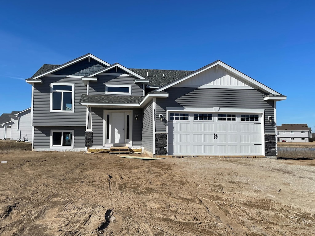 view of front of property featuring stone siding, driveway, a shingled roof, and a garage