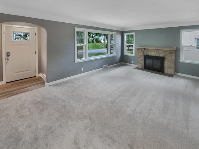 unfurnished living room with a stone fireplace and light carpet