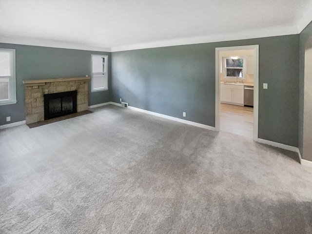 unfurnished living room featuring sink, light colored carpet, and a stone fireplace