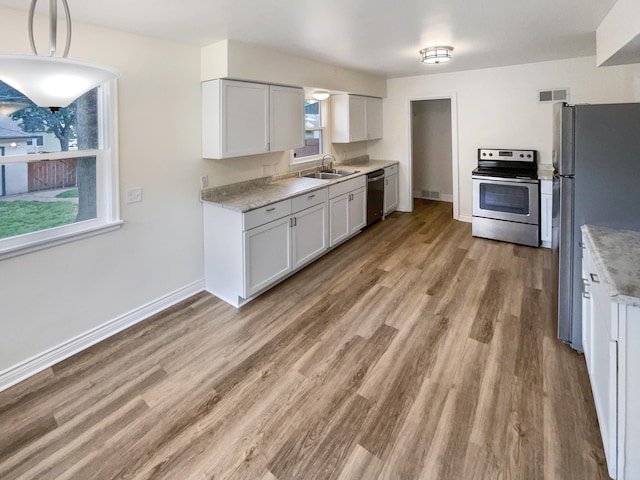 kitchen featuring appliances with stainless steel finishes, light hardwood / wood-style flooring, hanging light fixtures, and sink