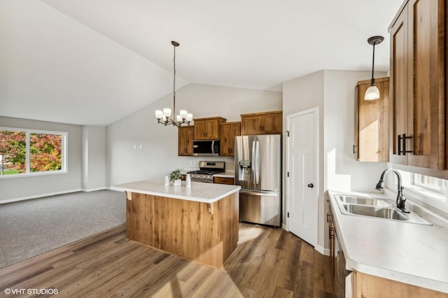 kitchen with stainless steel appliances, lofted ceiling, sink, a kitchen island, and decorative light fixtures