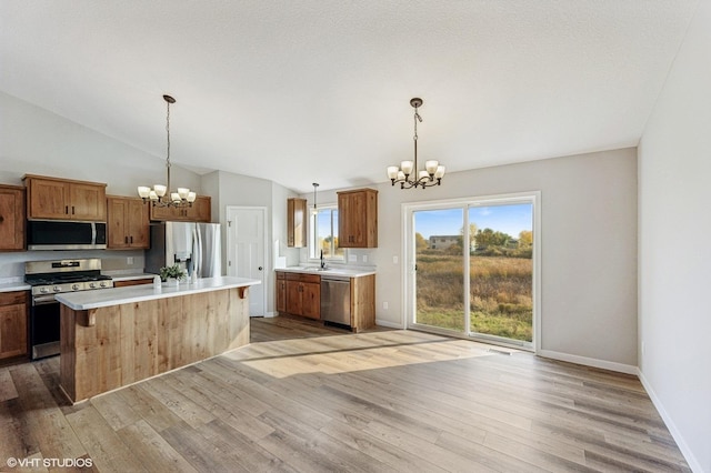 kitchen with a notable chandelier, appliances with stainless steel finishes, light hardwood / wood-style flooring, lofted ceiling, and a kitchen island