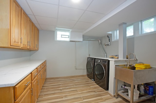 clothes washing area with cabinets, washing machine and dryer, sink, and light hardwood / wood-style flooring