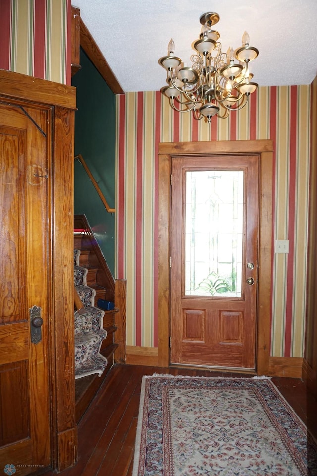 foyer with stairs, dark wood-style floors, an inviting chandelier, and wallpapered walls