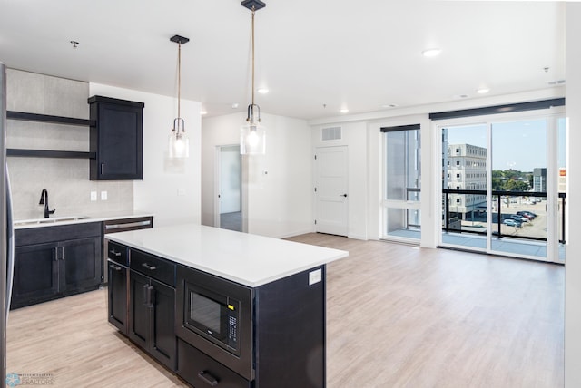 kitchen with decorative light fixtures, sink, light hardwood / wood-style floors, stainless steel microwave, and a center island