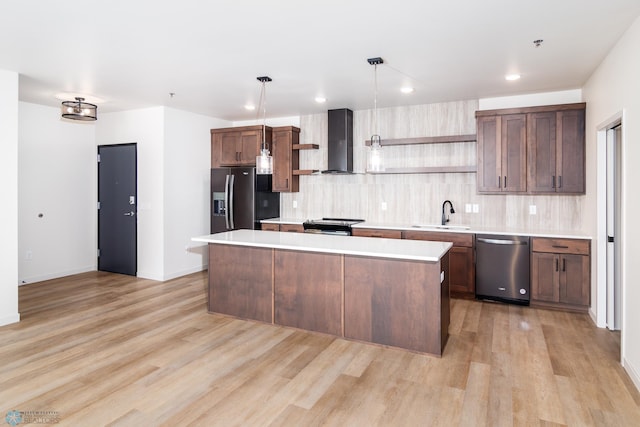 kitchen with a kitchen island, wall chimney range hood, stainless steel appliances, pendant lighting, and light wood-type flooring