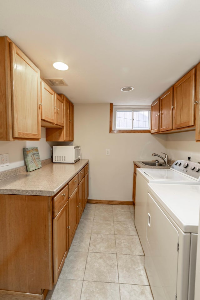 clothes washing area with sink, washing machine and dryer, light tile patterned floors, and cabinets