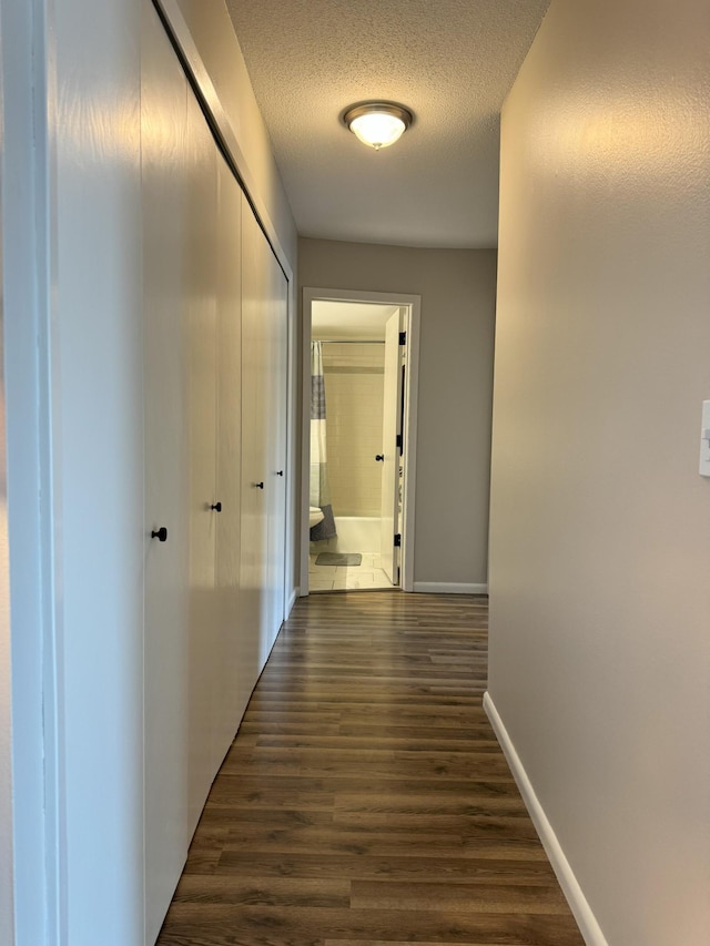 hall featuring dark wood finished floors, a textured ceiling, and baseboards