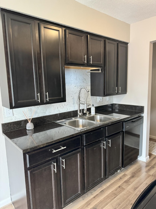 kitchen with black dishwasher, tasteful backsplash, dark stone counters, light wood-style flooring, and a sink