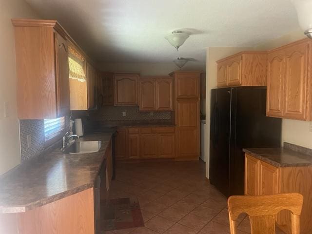 kitchen with dishwasher, light tile patterned flooring, sink, decorative backsplash, and black refrigerator