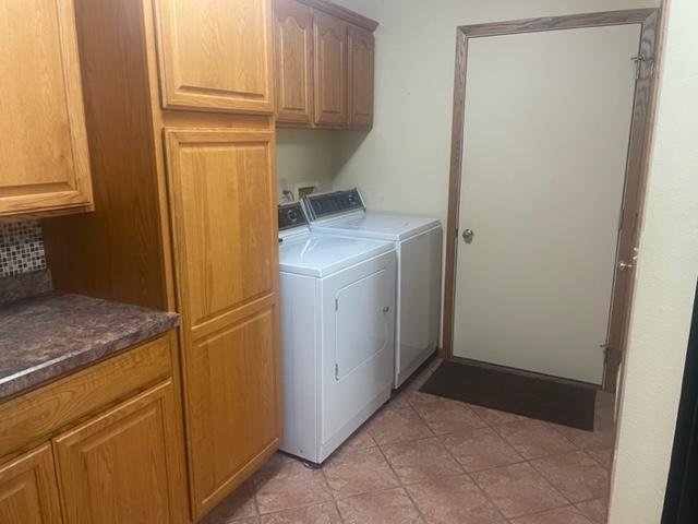 laundry area featuring washer and clothes dryer, light tile patterned floors, and cabinets