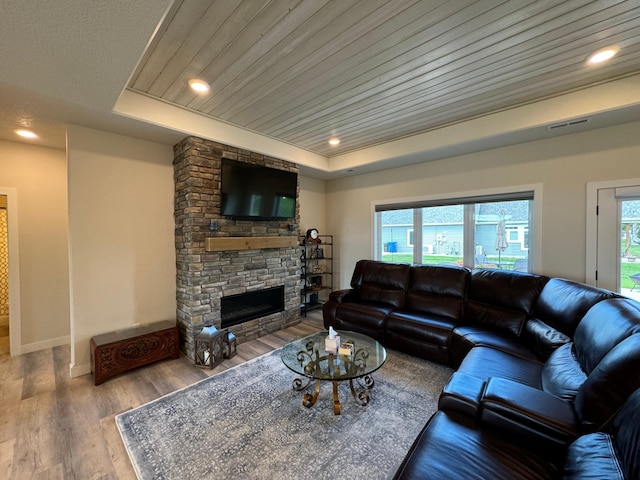 living room with a stone fireplace, wooden ceiling, a tray ceiling, a wealth of natural light, and hardwood / wood-style flooring